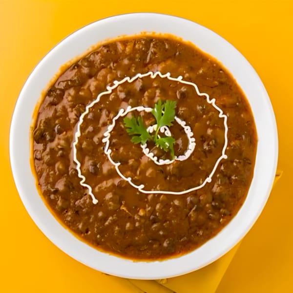 Tandoori Flame's Dal Makhani, a rich lentil dish, garnished with cream and cilantro on a white plate.