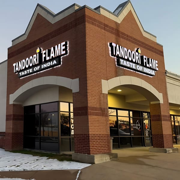 Exterior of Tandoori Flame, an Indian restaurant, with brick walls and illuminated signs at dusk.