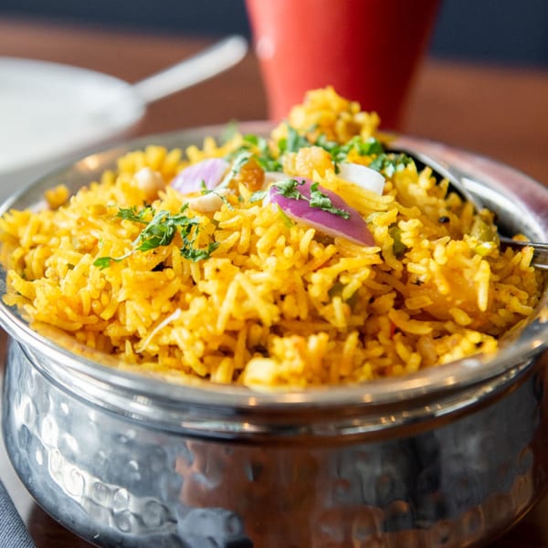 Close-up of Tandoori Flame's yellow Indian rice pilaf with red onions and cilantro in a metal bowl.