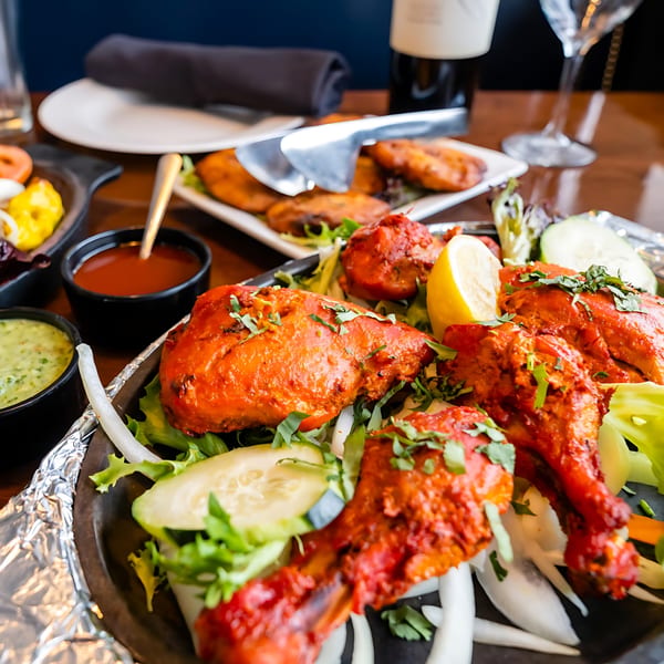 Tandoori Flame's vibrant Tandoori Chicken, garnished with lemon and cilantro, served with chutneys.