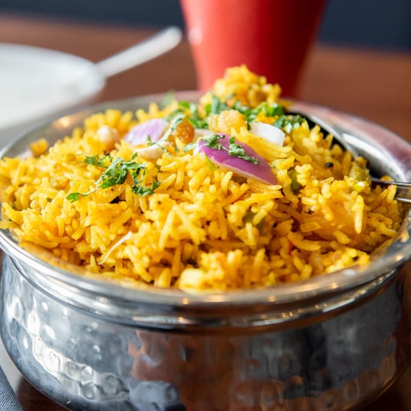 Close-up of Tandoori Flame's yellow biryani rice, garnished with red onions and cilantro in a metal bowl.