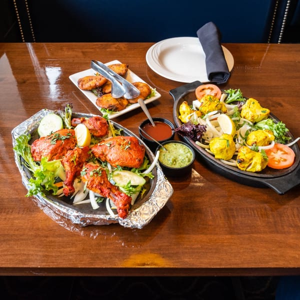 Two sizzling platters of Tandoori Flame's chicken tikka and tandoori chicken, with sides and sauces.