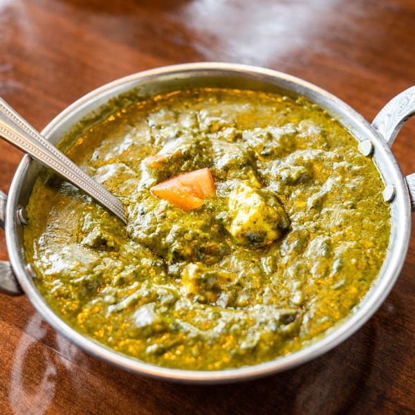 A metal bowl of vibrant green Palak Paneer, an Indian spinach and cheese curry, with a spoon.