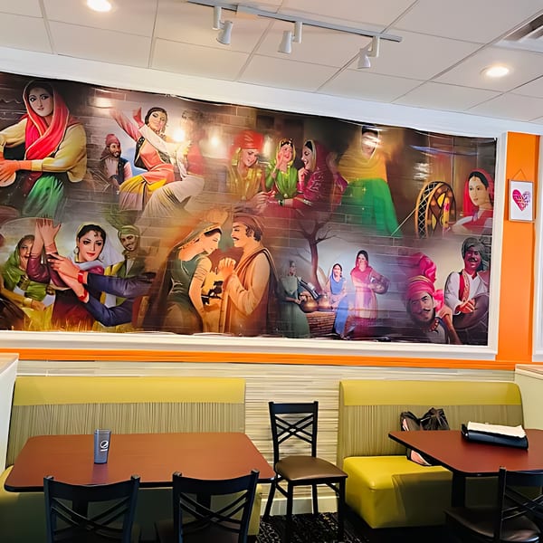 A vibrant mural depicting Indian cultural scenes adorns the wall above restaurant booths and tables.