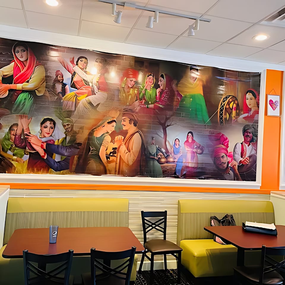 A vibrant mural depicting Indian cultural scenes adorns the wall above restaurant booths and tables.