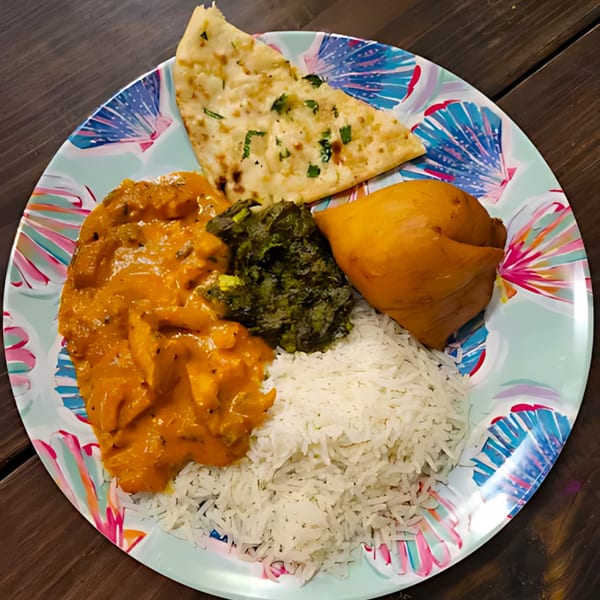 A colorful plate of Indian food with butter chicken, rice, palak paneer, naan, and a samosa.