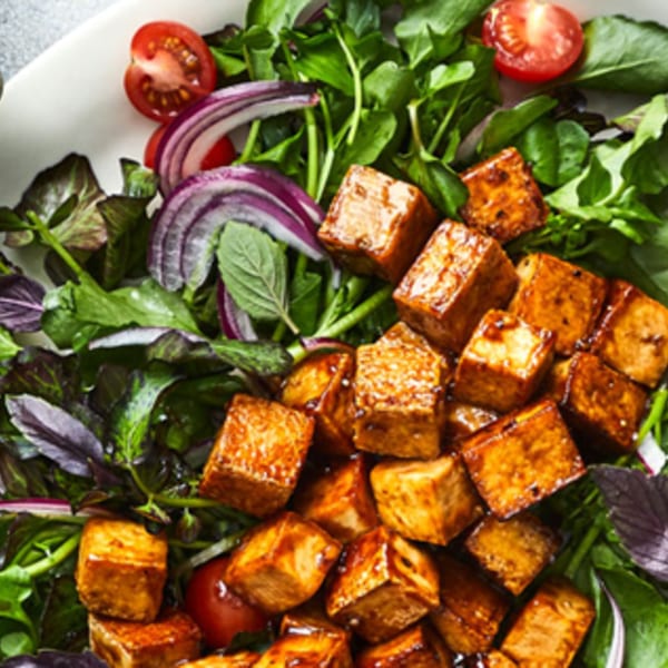 Close-up of a vibrant salad with golden paneer cubes, fresh greens, red onions, and cherry tomatoes.