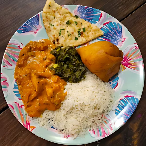 A colorful plate of Indian food with butter chicken, rice, naan, saag, and a samosa.