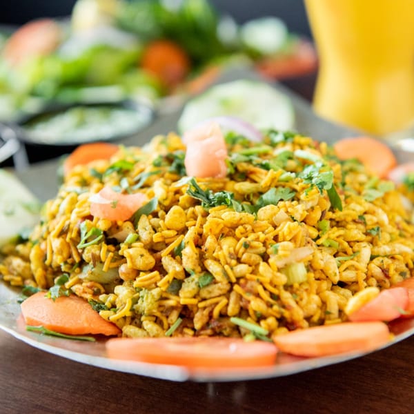 Close-up of a Tandoori Flame Bhel Puri dish, garnished with cilantro, tomatoes, and onions.