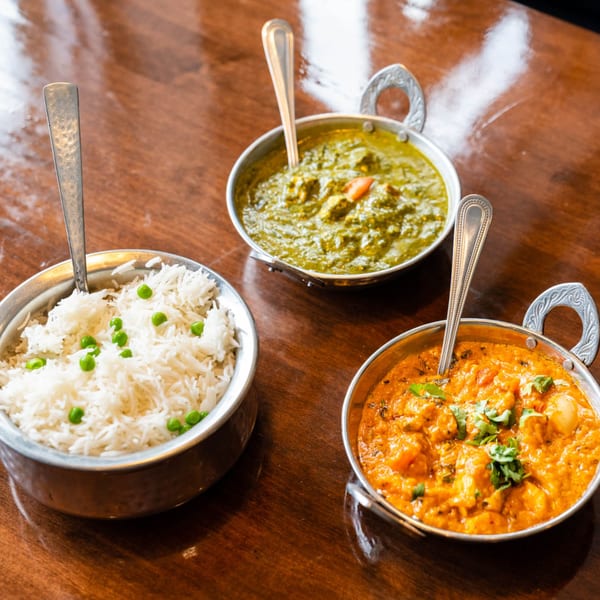 Three Indian dishes: rice with peas, green spinach curry, and orange chicken curry in metal bowls.