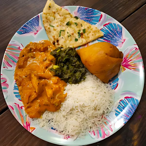 A colorful plate of Tandoori Flame's Indian food, including butter chicken, rice, naan, saag, and a samosa.